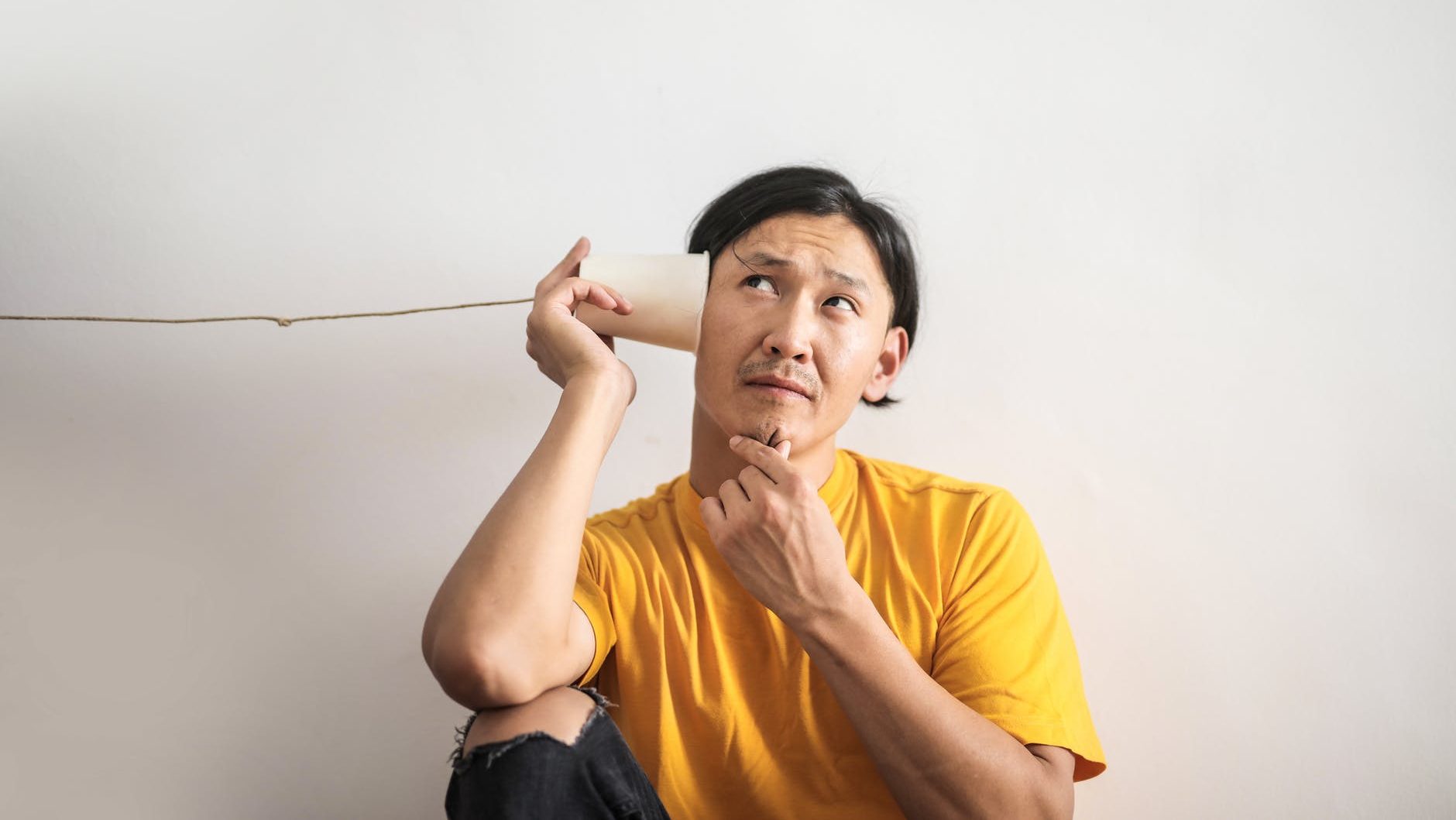 pensive ethnic man listening to answer in paper cup phone